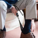 Un homme âgé utilise un chausse-pied pour mettre sa chaussure.