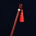 Gros plan d'une canne en bois brun foncé avec un gland rouge.