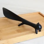 Black cat-shaped spatula on a wooden tray. Unique kitchen gadget.