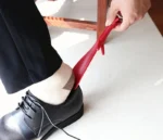 Personne utilisant un chausse-pied rouge pour enfiler une chaussure noire.