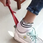 Personne utilisant un chausse-pied rouge pour enfiler une basket blanche.