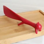 Red cat-shaped butter knife on a wooden tray.